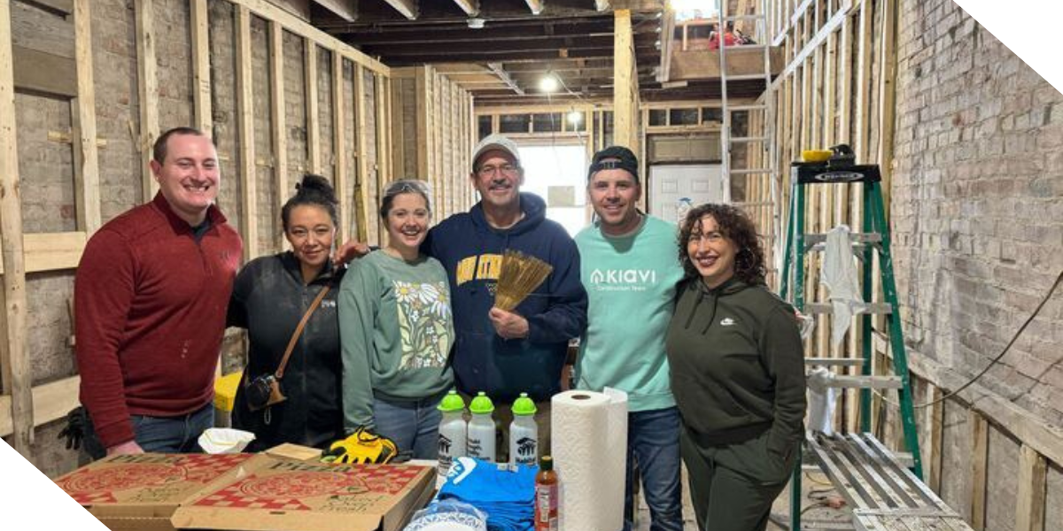 Six Kiavi employees smiling in an unfinished room, helping build a row house with Habitat for Humanity of Greater Pittsburgh.