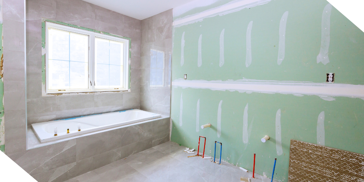  A modern bathroom under construction with a white bathtub, partially tiled walls, and exposed plumbing.