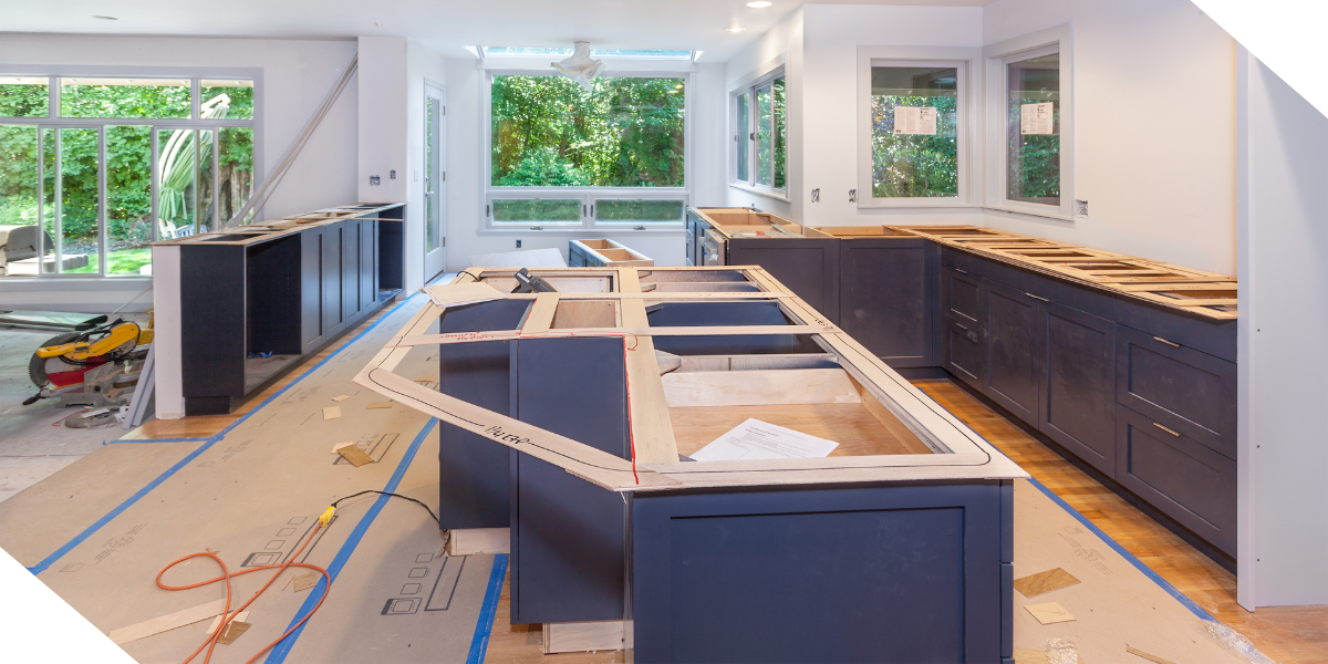 A kitchen under renovation with dark cabinets and wooden floors, sunlight streaming in through windows. 