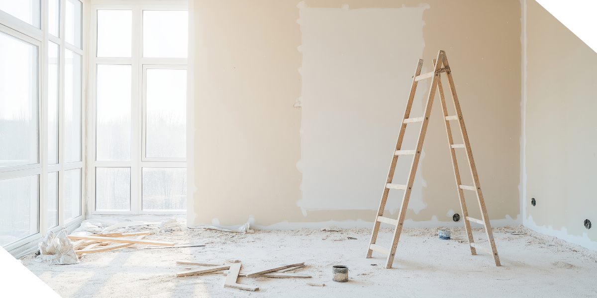 A wooden ladder stands on a dusty floor in a room with large windows, renovation debris scattered around. 