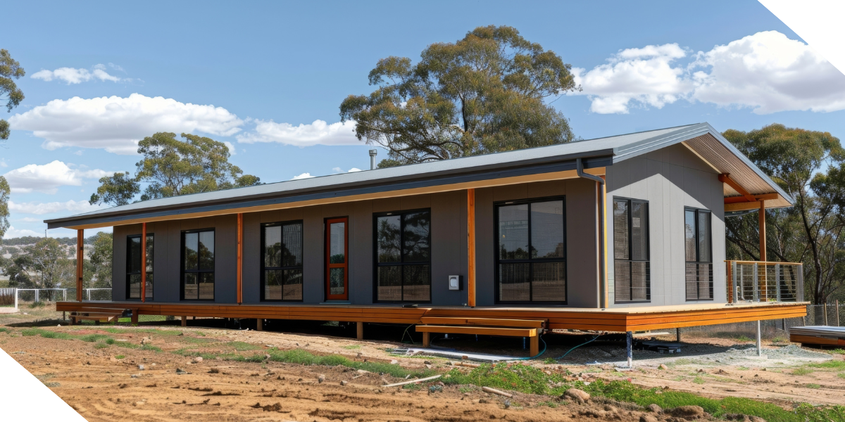 Modern modular one-story house with large windows and a wooden deck, surrounded by trees.