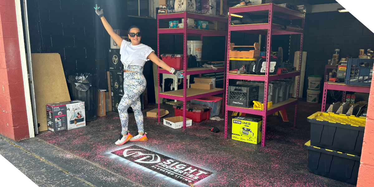 Michelle Jimenez, a real estate investor based out of Pittsburgh, PA stands in a garage filled with supplies and her company logo, Sight Properties, is painted on the ground.