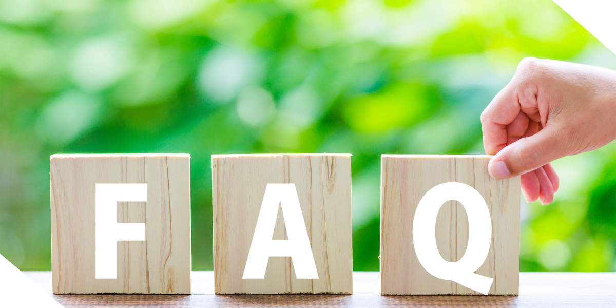 A real estate agents hand placing a wooden block labeled "Q" next to "F" and "A" blocks to spell "FAQ" against a blurred green background.