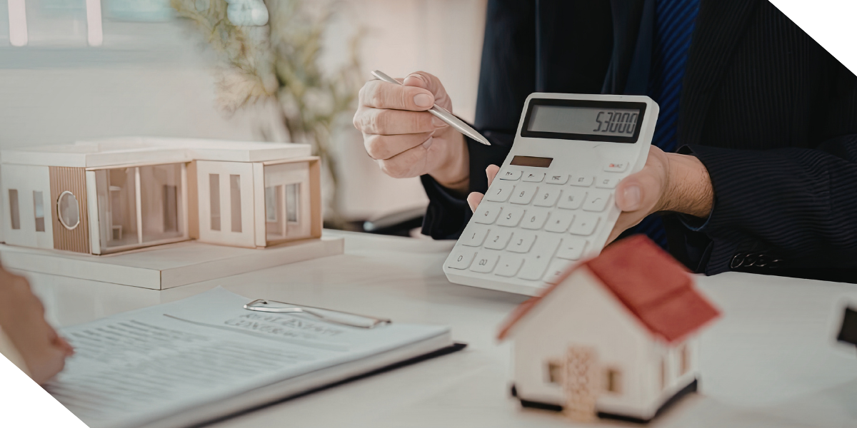 Real estate investor using a calculator next to house models and a contract to calculate renovation costs and potential return on investment (ROI).