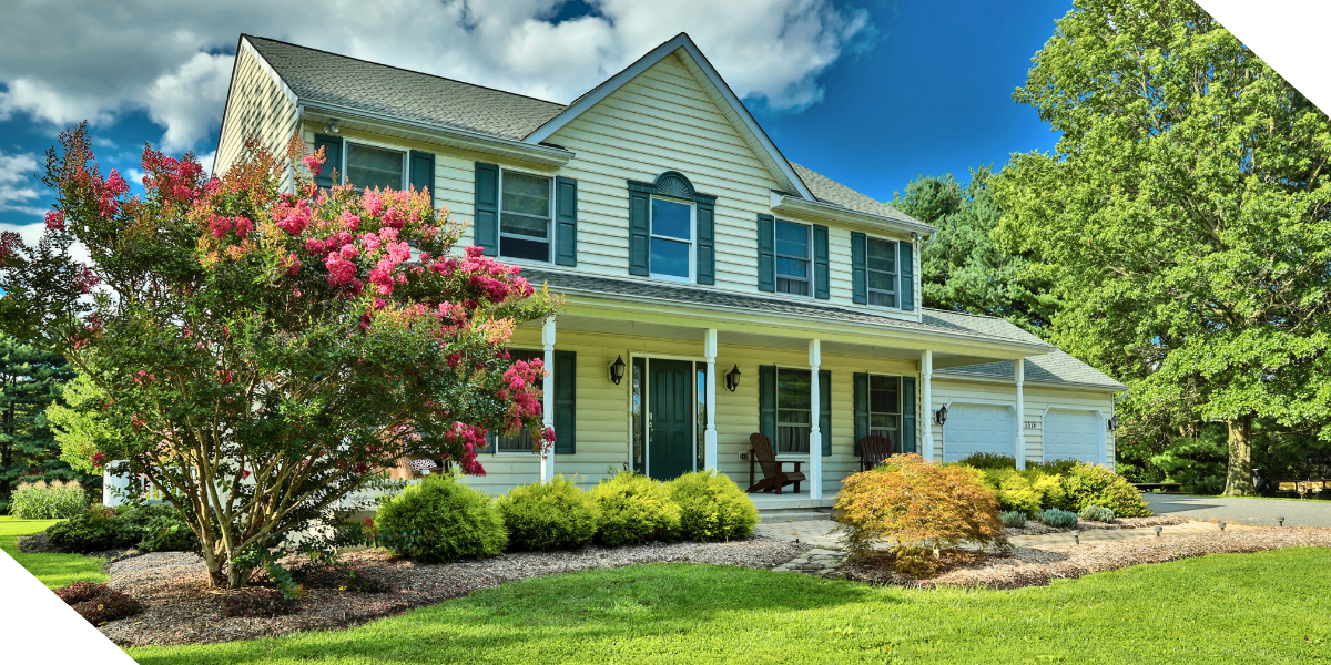 Exterior of a two-story residential home with professional landscaping, featuring a blooming crepe myrtle tree and manicured shrubs to increase curb appeal for a fix-and-flip project.