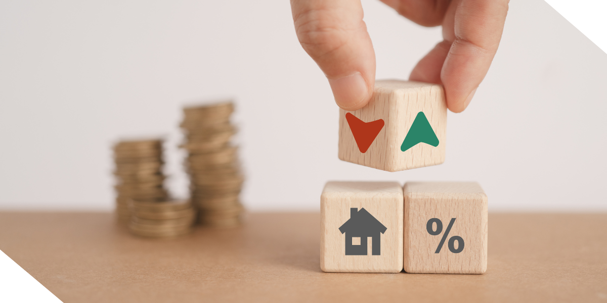 A hand of a real estate investor placing wooden blocks with upward and downward arrows, a house, and a percentage sign. Stacks of coins are in the background.