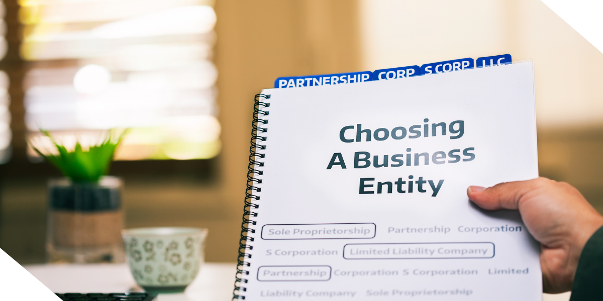 A real estate investors hand holding a spiral-bound guide titled 'Choosing A Business Entity' with business types listed. 