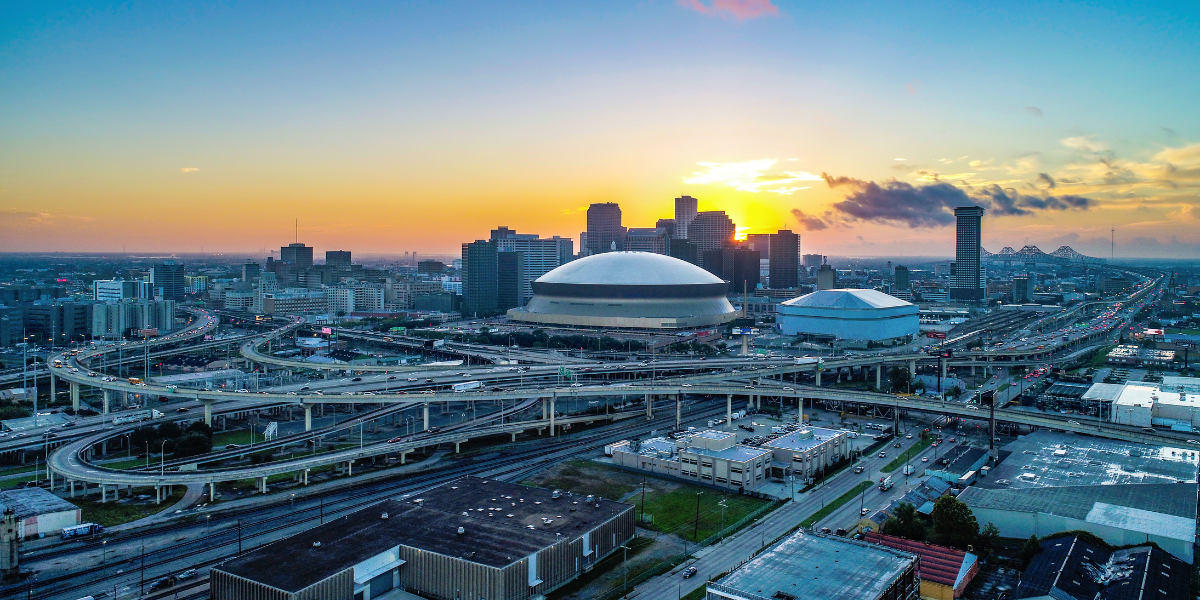 Sunset aerial view of the New Orleans skyline featuring the Superdome and a busy highway interchange.