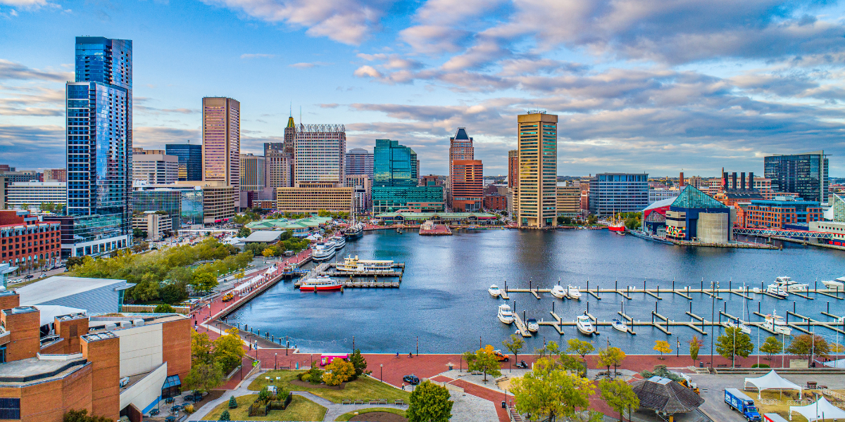 Aerial view of Baltimore's Inner Harbor featuring skyscrapers, calm water, and docked boats under a cloudy sky.