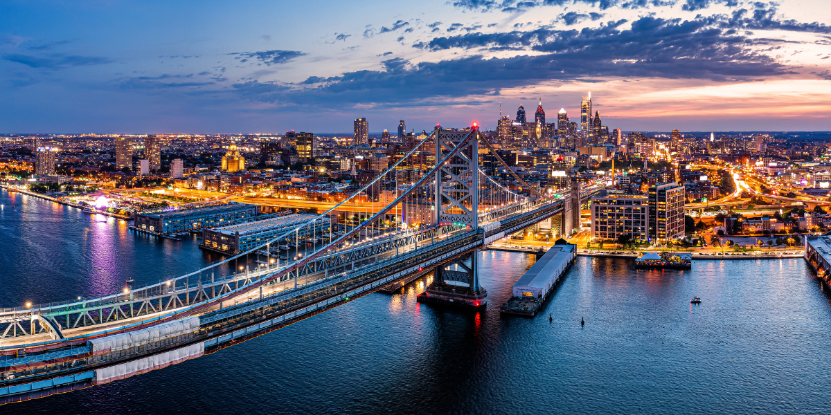 The Philadelphia skyline and Benjamin Franklin Bridge illuminated at night over the Delaware River.