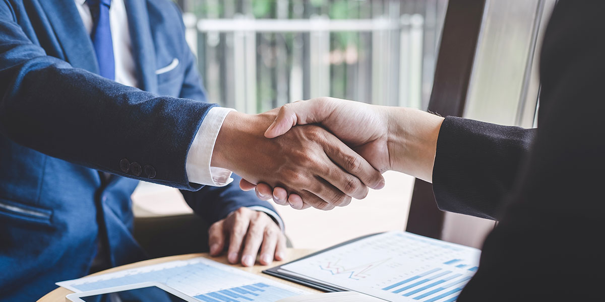 Two people in suits shaking hands over a desk for a fix and flip deal