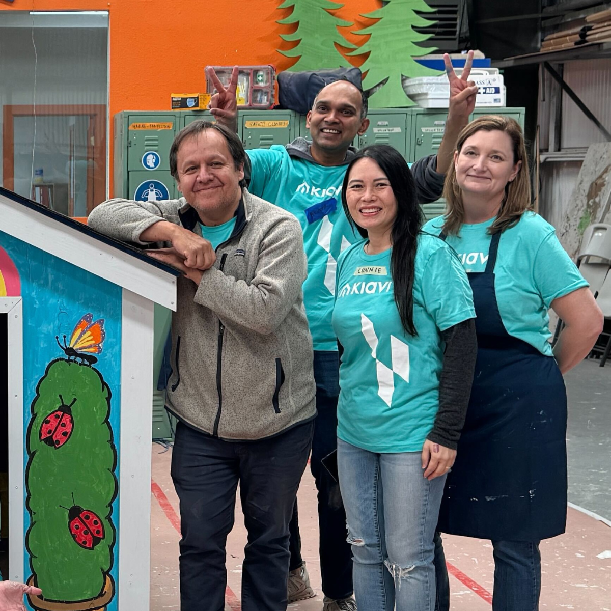 Kiavi employees in Kiavi shirts participating in a Habitat for Humanity build, smiling and posing with a house decoration.