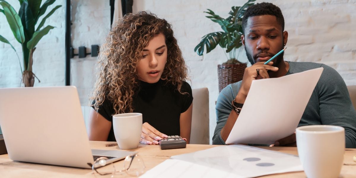 Two focused real estate investors analyzing financial documents and calculating house flipping costs on their laptops