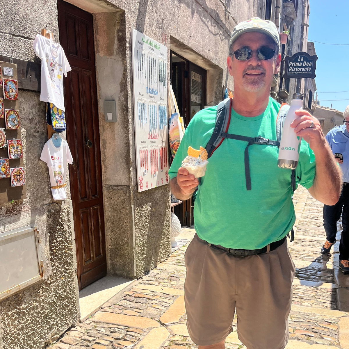 A Kiavi employee in a green shirt holds ice cream and a water bottle while walking down a cobblestone street.