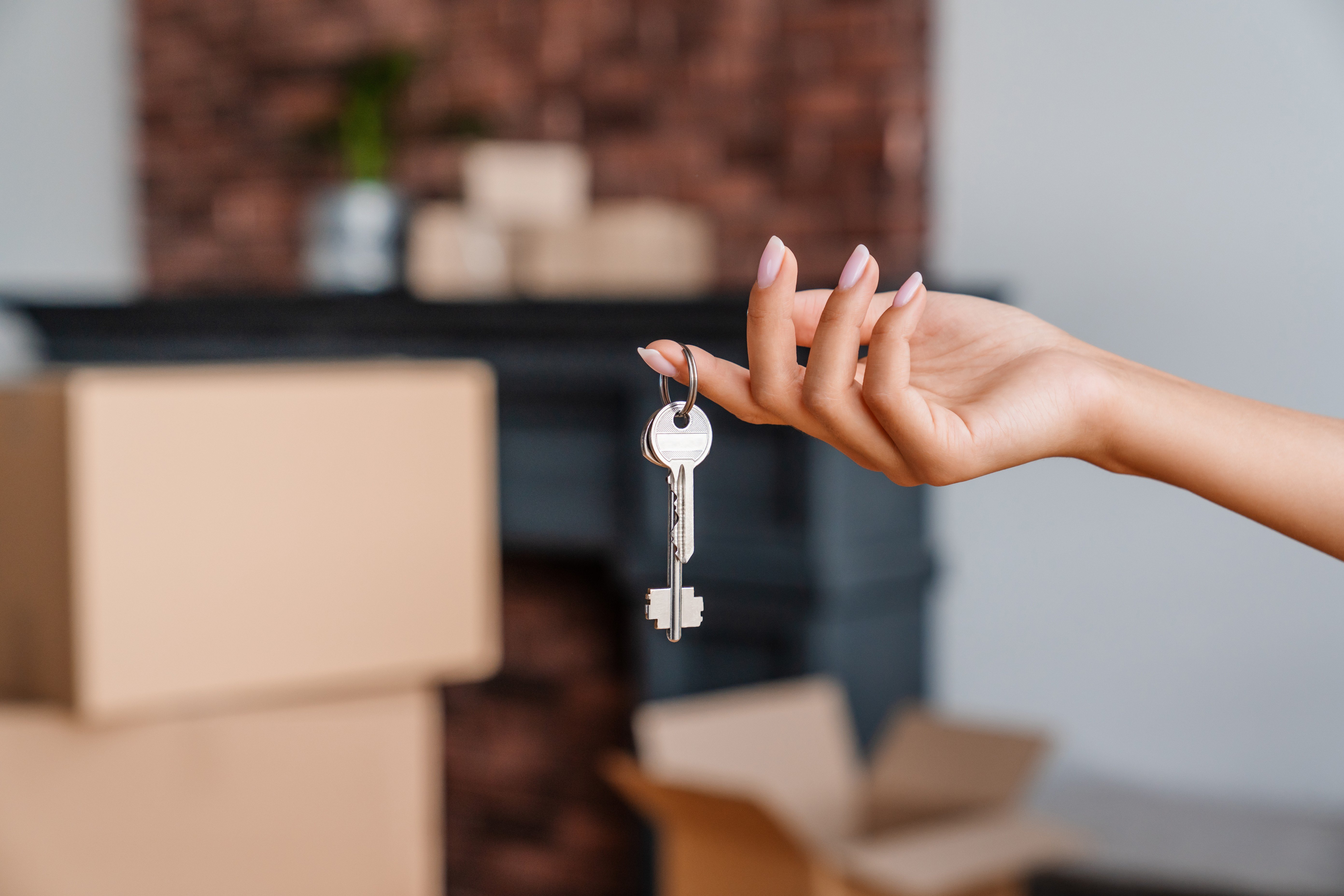 A hand holding a key with several cardboard boxes in the background.