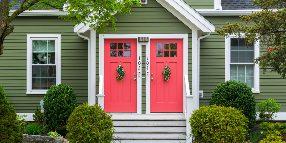A green duplex with two red doors, ideal for house hacking and real estate investing with Kiavi financing.