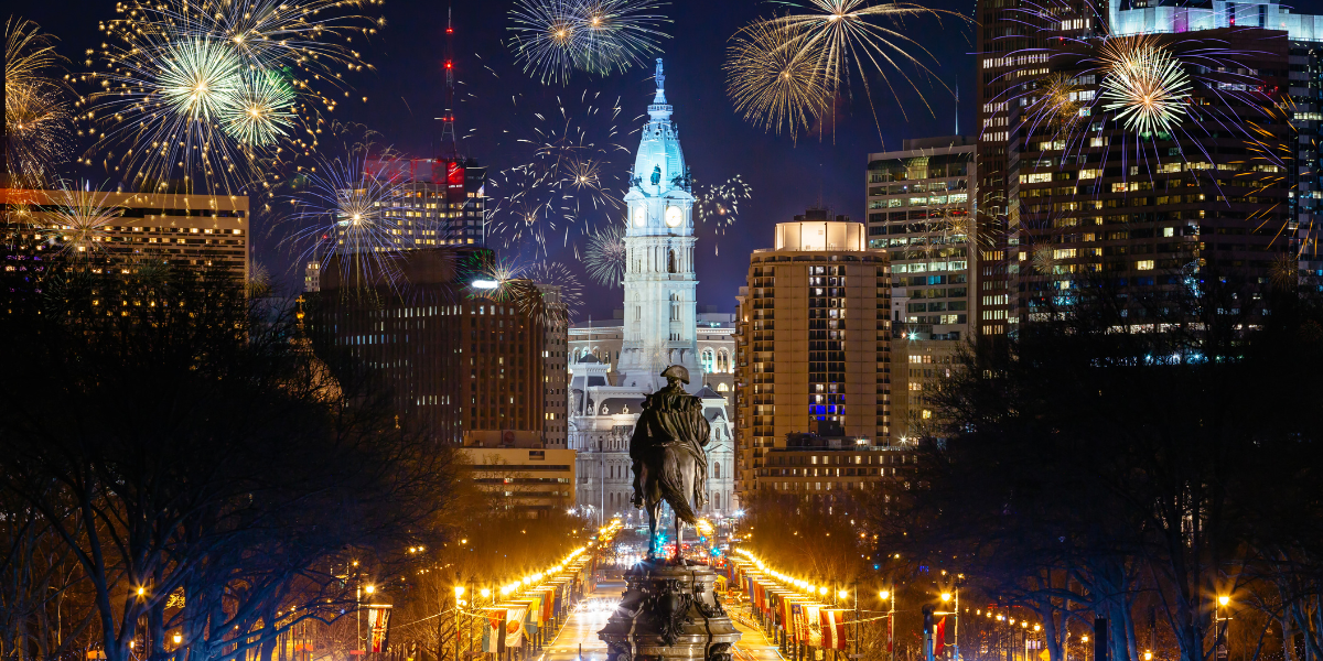Nighttime view of Philadelphia City Hall and the William Penn statue under a sky filled with fireworks.