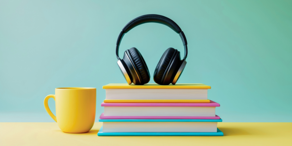 A stack of colorful books with black headphones on top and a yellow mug beside them.