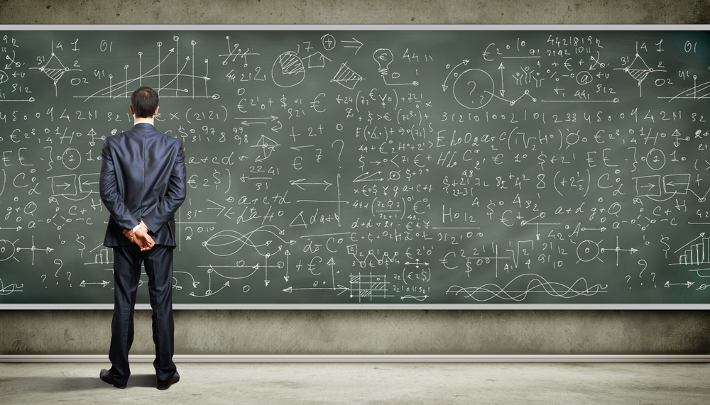 A man with his back to the camera standing in front of a blackboard with math equations on it.