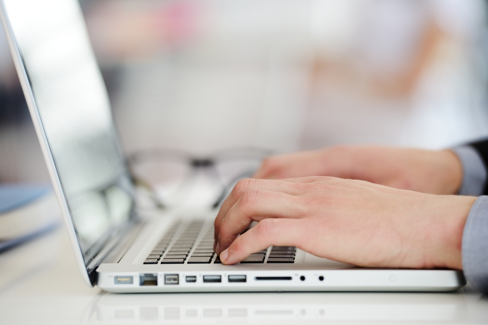 A closeup of a man's hands on a laptop.