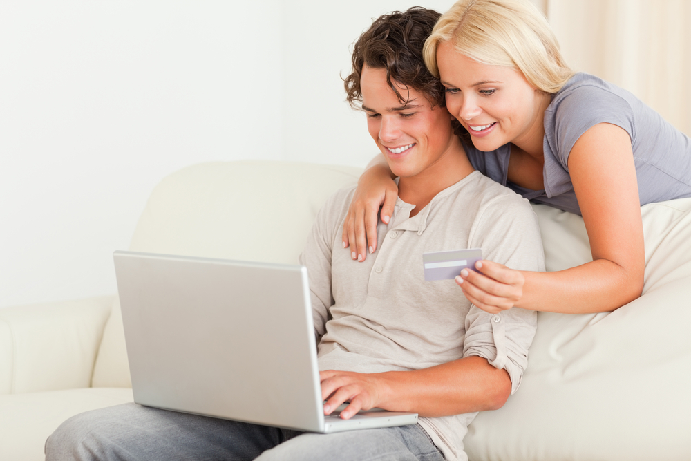 A couple on a couch looking at a laptop and trying to find a house to flip.