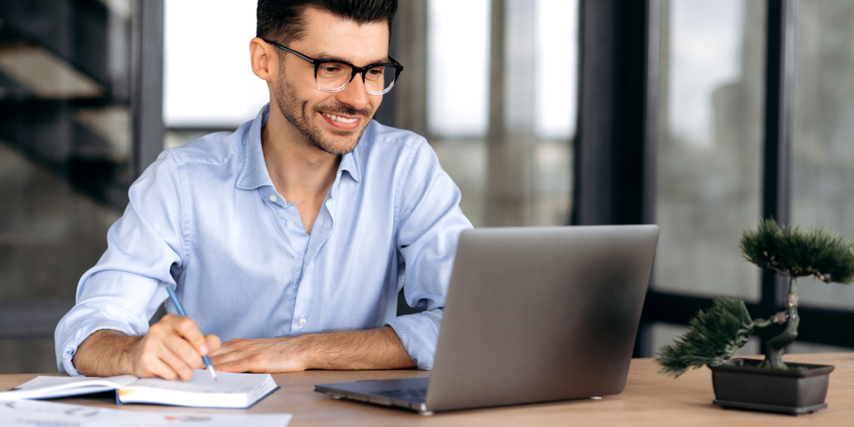 male real estate investor smiling as he works on a laptop