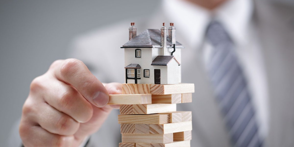 close up of a real estate investor balancing a tower of wood blocks with a tiny model house on top