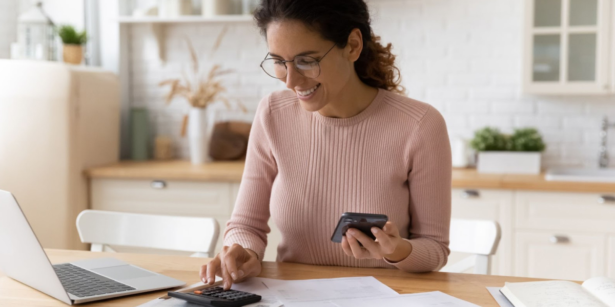 smiling female real estate investor sitting at a table reviewing paperwork with a calculator