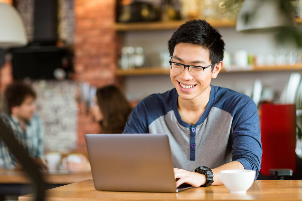 A man smiling at a laptop in a cafe.