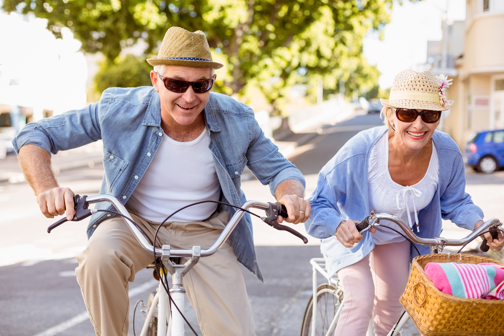 An elderly couple in matching outfits smiling and riding bikes together.