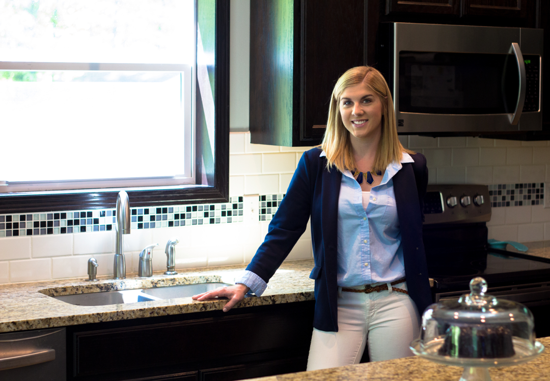A well-dressed blonde girl in a kitchen who is a real estate professional.
