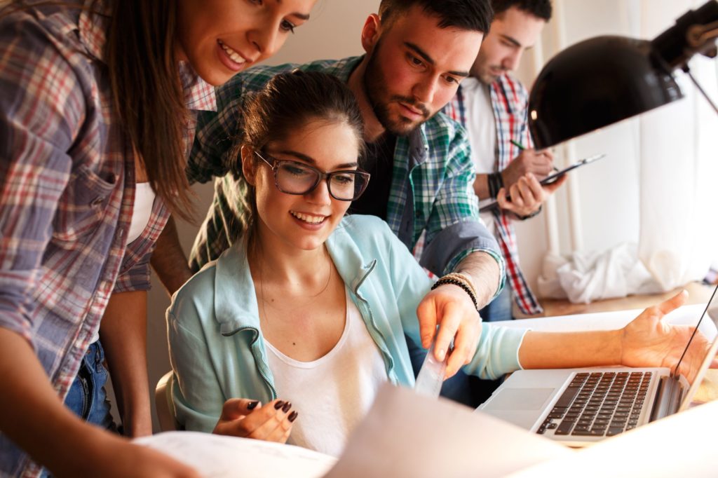 A group of young people looking at papers over a laptop at a desk.