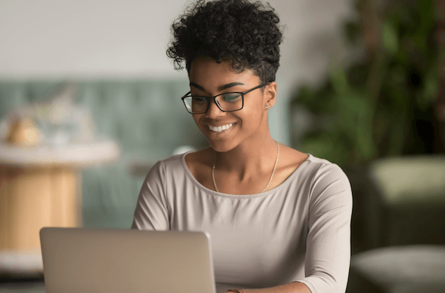 A smiling woman with glasses looking at a laptop and researching real estate investing.