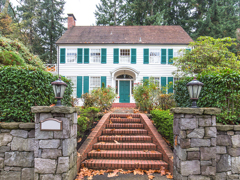 The entrance of a white home with green shutters and a brick stair walkway.