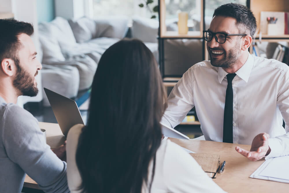 A man in a suit explaining a business proposal to a couple at a table.