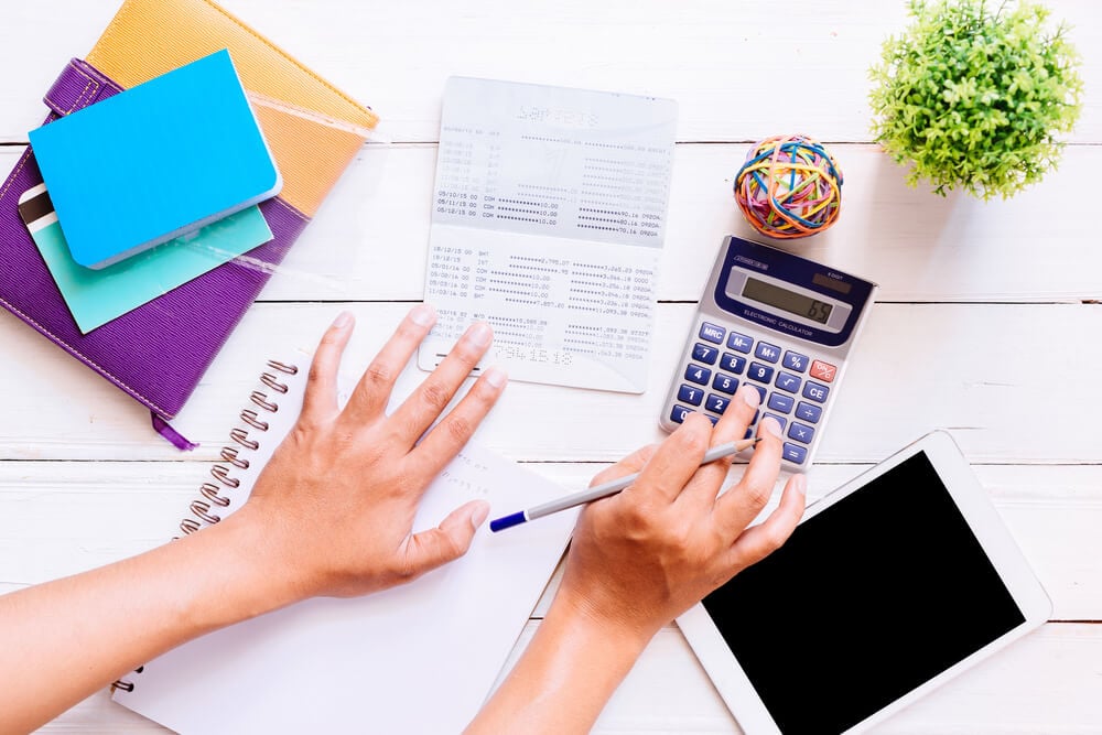 An overlay of s woman's hands working on a calculator with notebooks and a plant.