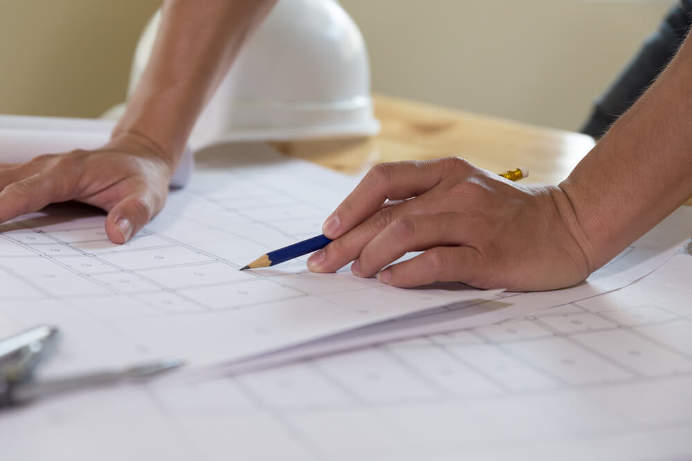 A person's hands holding a pencil and going over a blueprint of a construction site.