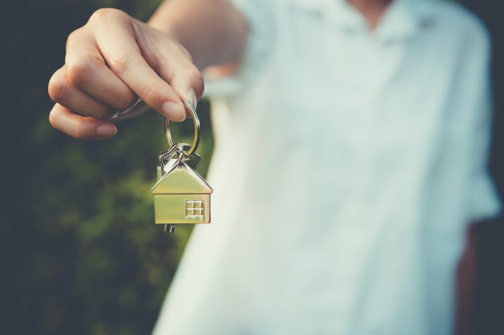 A person holding up a keychain of a home.