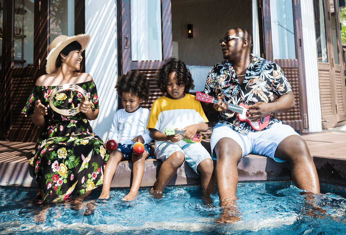 A happy family of four wearing Hawaiian clothes and wading in a little pool.