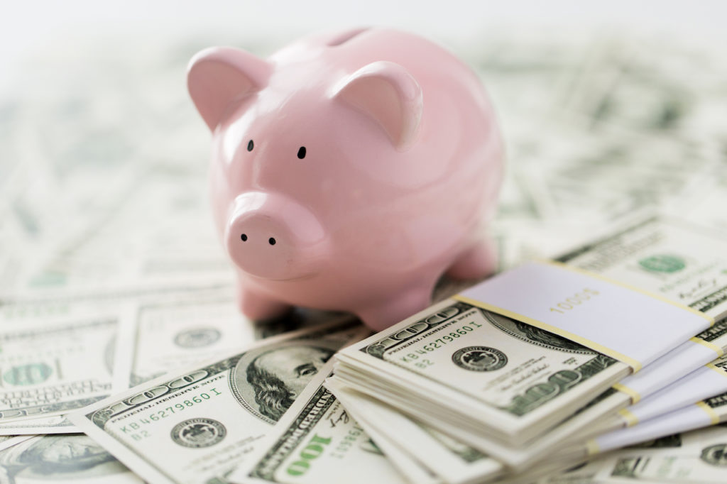 A pink piggy bank on top of a pile of money for real estate investing.