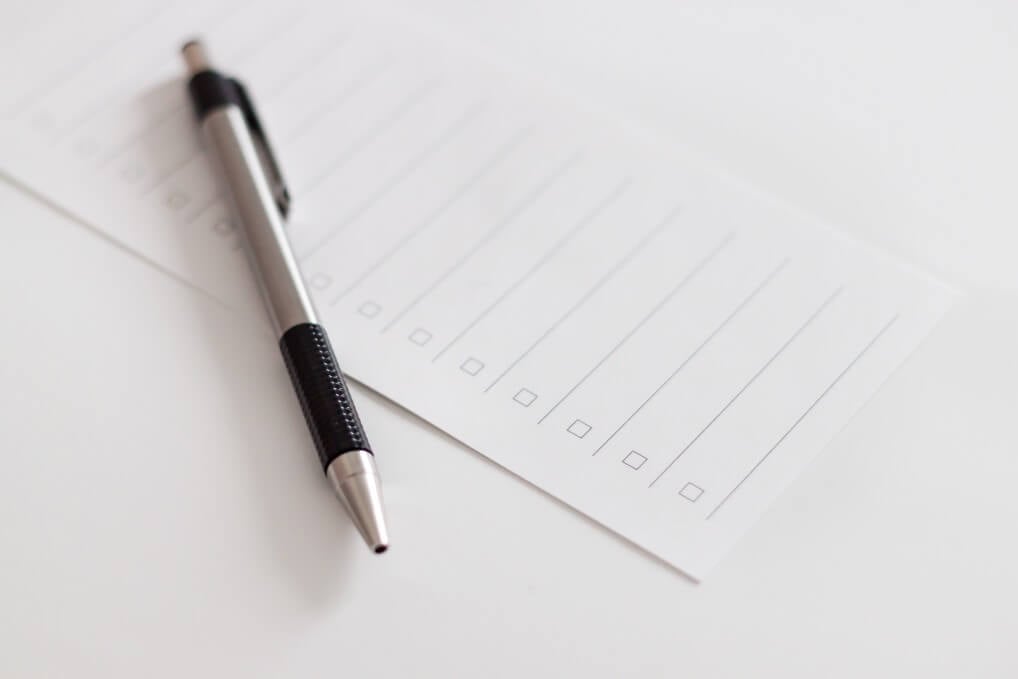 A pen next to a blank piece of paper on a white table.