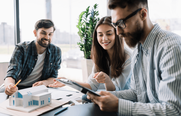 A group of people at a desk with a model home on it looking over a clipboard.