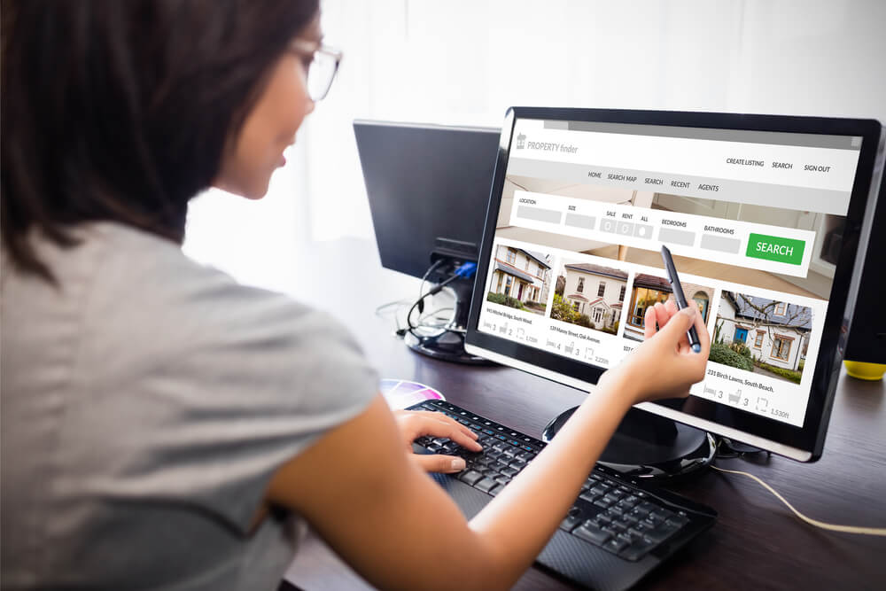 A woman in glasses shopping for real estate investing homes on a computer.