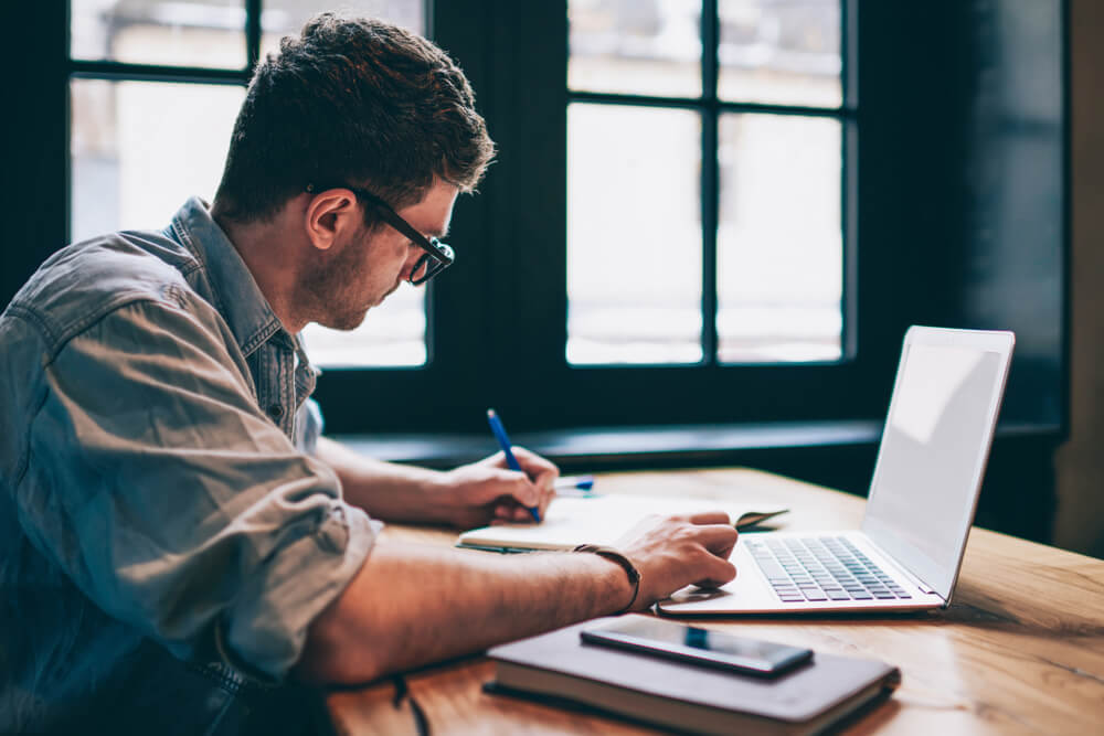 A man doing work at a desk in front of his laptop.