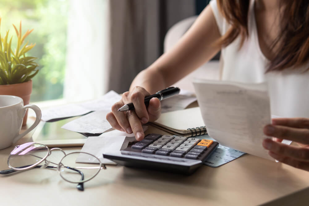 A woman's hand doing math on a calculator while holding up a sheet of paper.