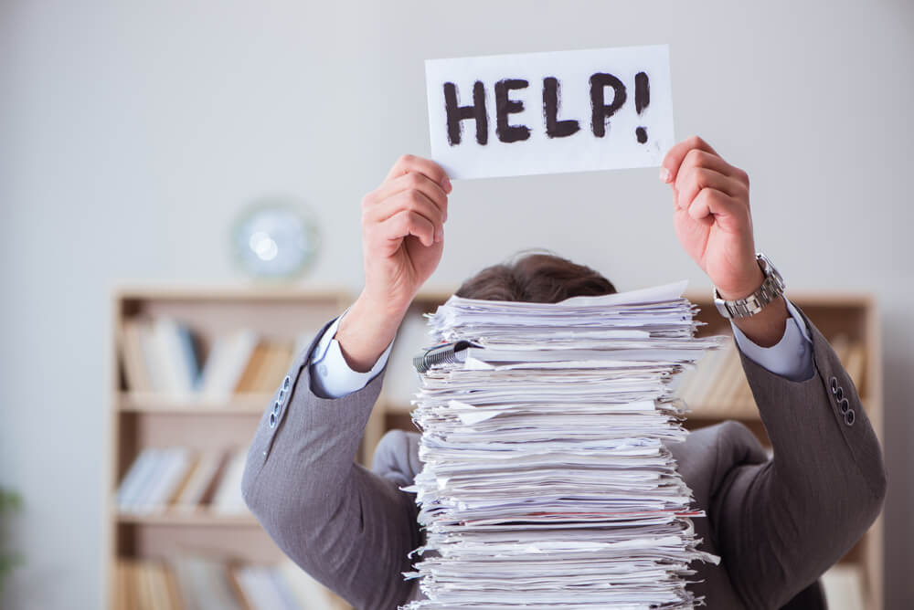 A man with a pile of papers in front of him in an office holding up a 