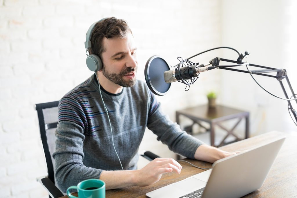 A man in front of a microphone hosting a podcast with headphones on.