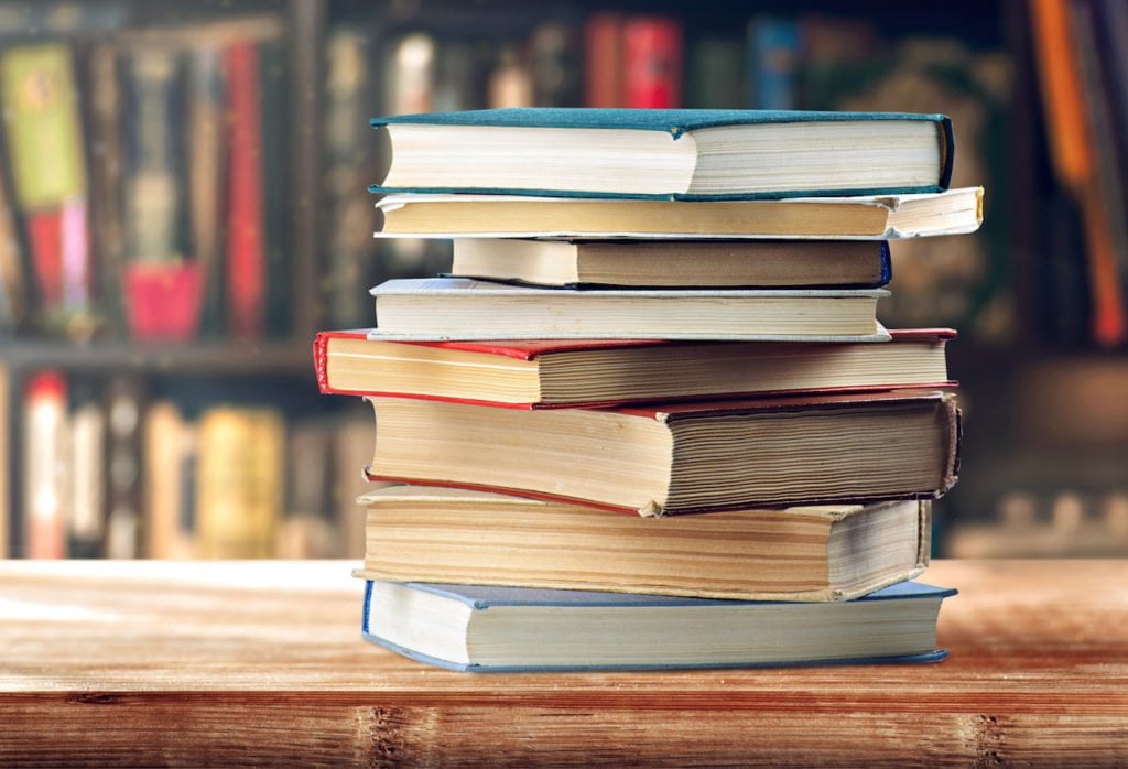 A stack of books about real estate investing on a wood table in a library.