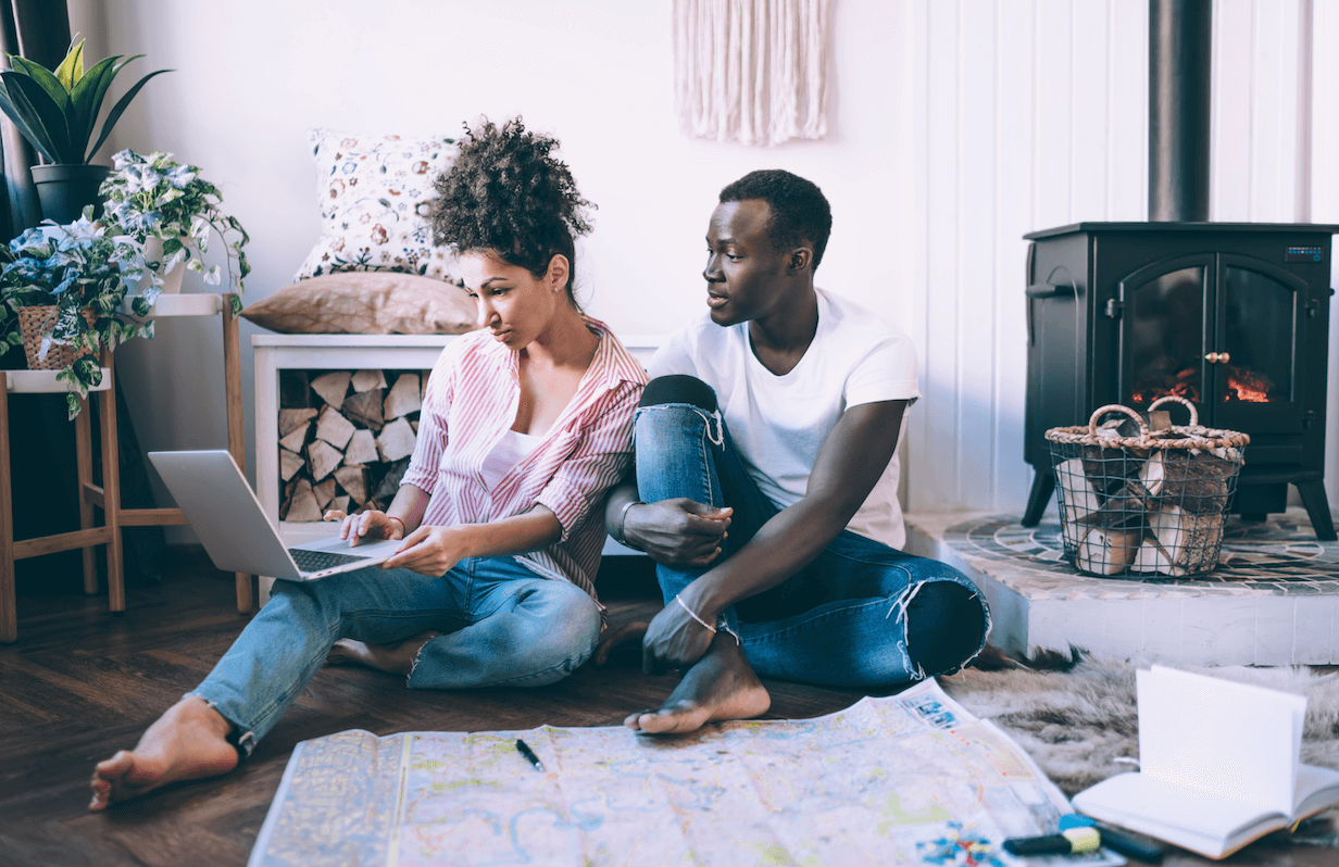 A couple in a house on the floor with a laptop researching vacation rentals.