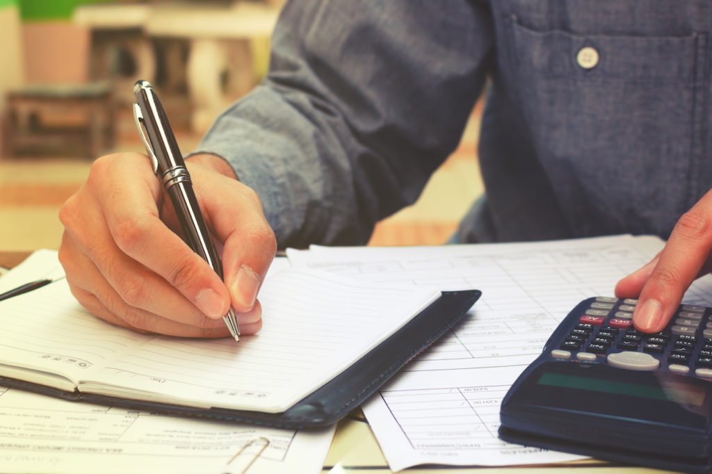 A closeup on a hand writing on a pad of paper and a calculator.